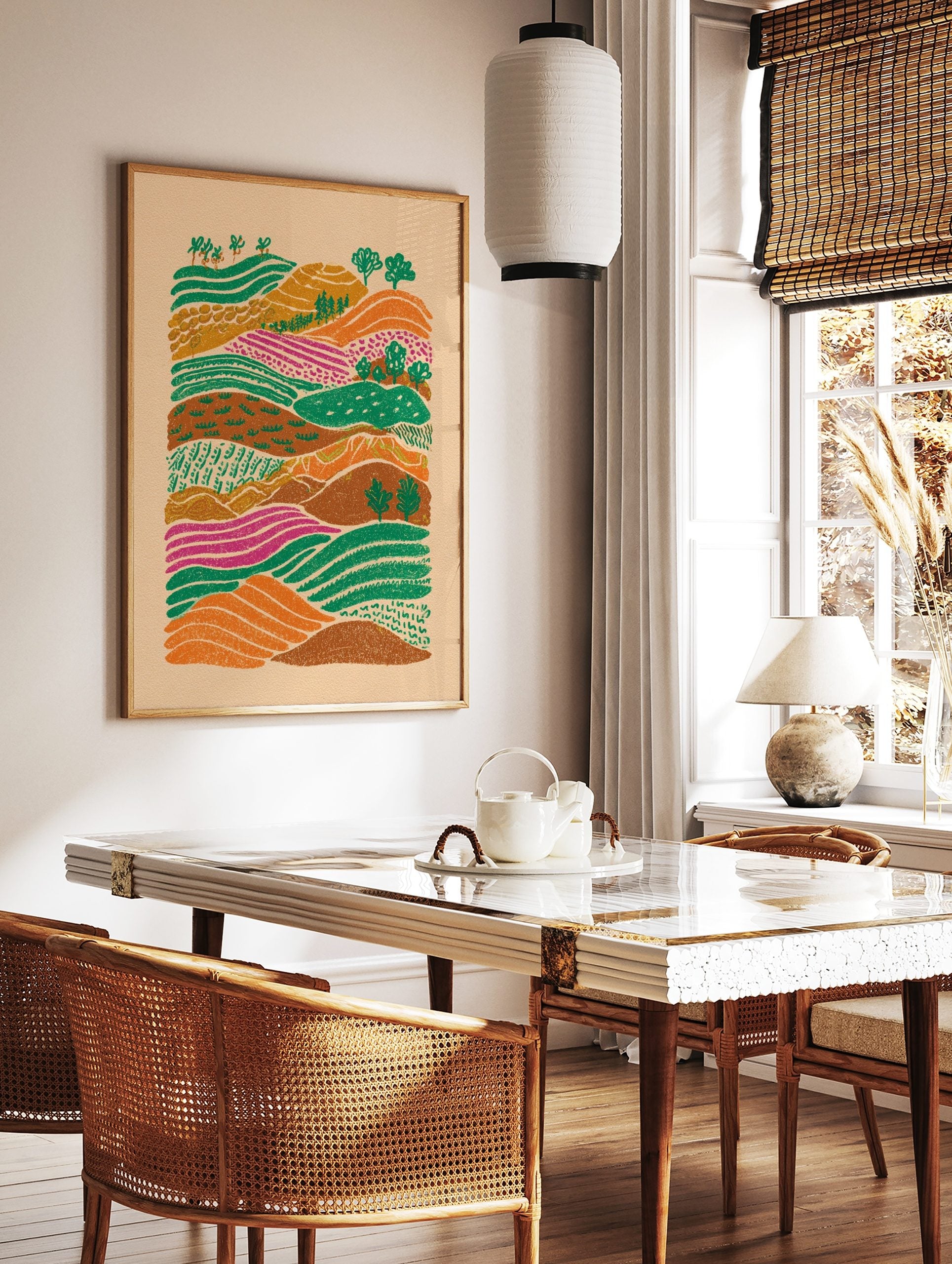 Colourful illustrative landscape art print with rolling hills, patterned green, orange, and magenta, in a styled room mockup