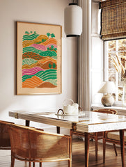 Colourful illustrative landscape art print with rolling hills, patterned green, orange, and magenta, in a styled room mockup