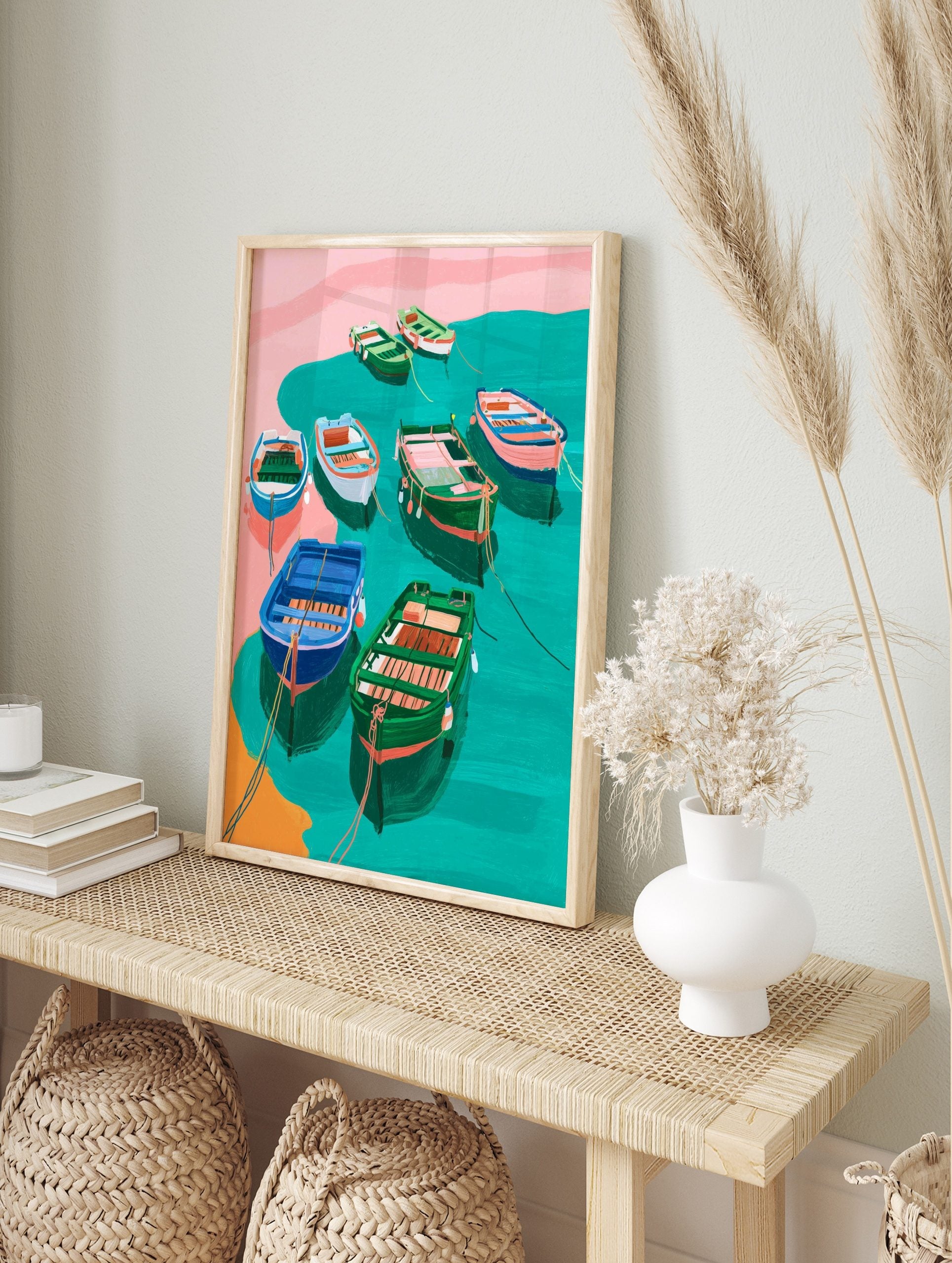 Illustrative art print of colourful fishing boats in teal water with pink shore and orange, in an alternate framed mockup