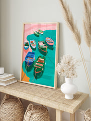 Illustrative art print of colourful fishing boats in teal water with pink shore and orange, in an alternate framed mockup