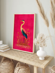Illustrative heron bird with yellow, red, and blue feathers standing in reeds on a fuchsia, in an alternate framed mockup