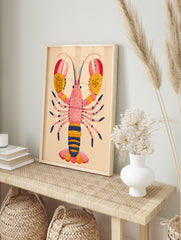 Illustrative lobster art print with pink body, yellow and red dotted claws, and navy accents, in an alternate framed mockup