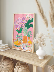 Colourful illustrative still life print with pink orchids, pineapples, mangoes, and patterned, in an alternate framed mockup