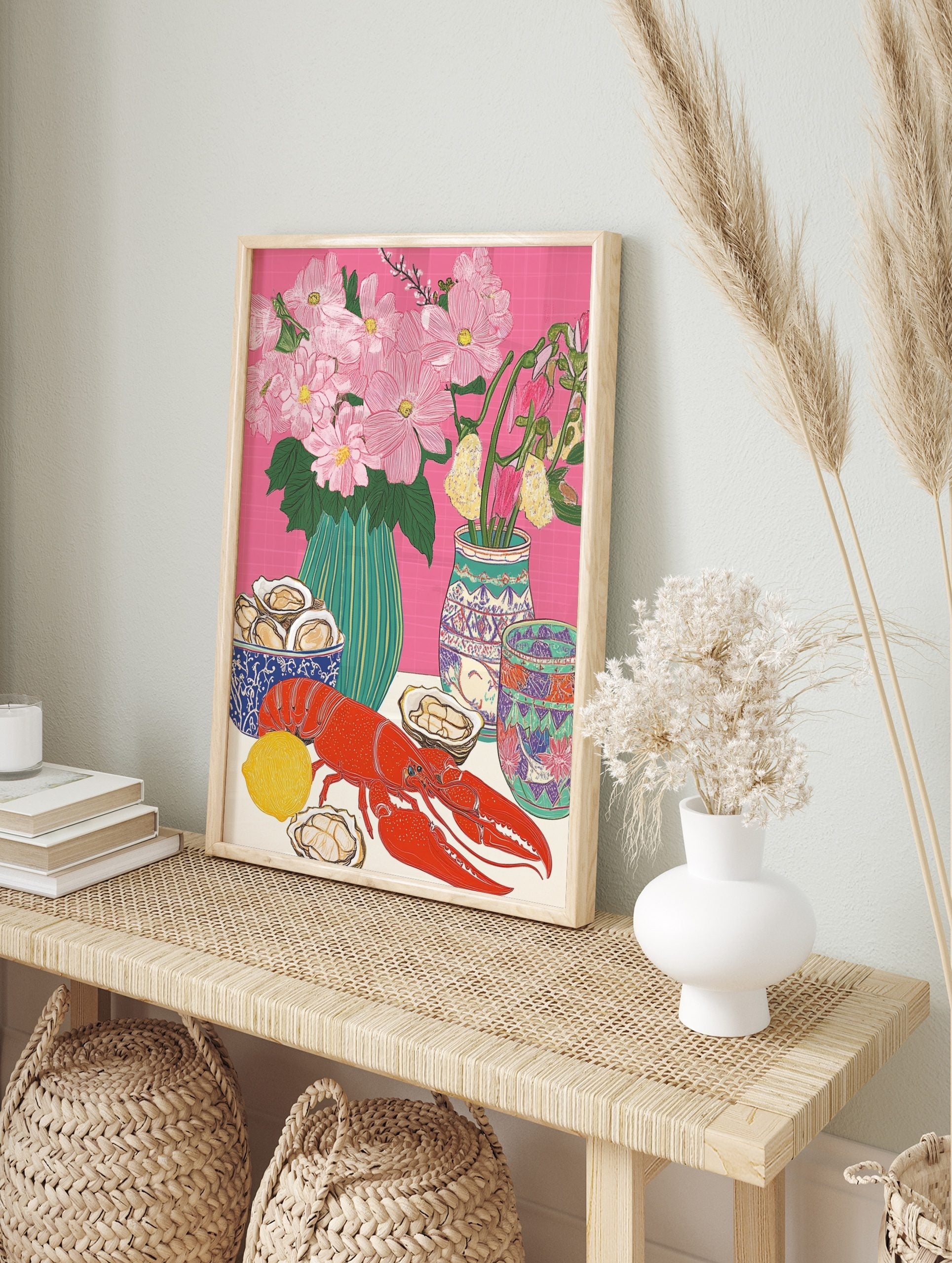 Illustrative still life print of a red lobster, oysters, lemon, and pink flowers in vases on, in an alternate framed mockup