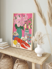 Illustrative still life print of a red lobster, oysters, lemon, and pink flowers in vases on, in an alternate framed mockup