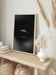 Monochrome stipple print of a cosmic eye with stars on a black background, unframed wall art, in an alternate framed mockup