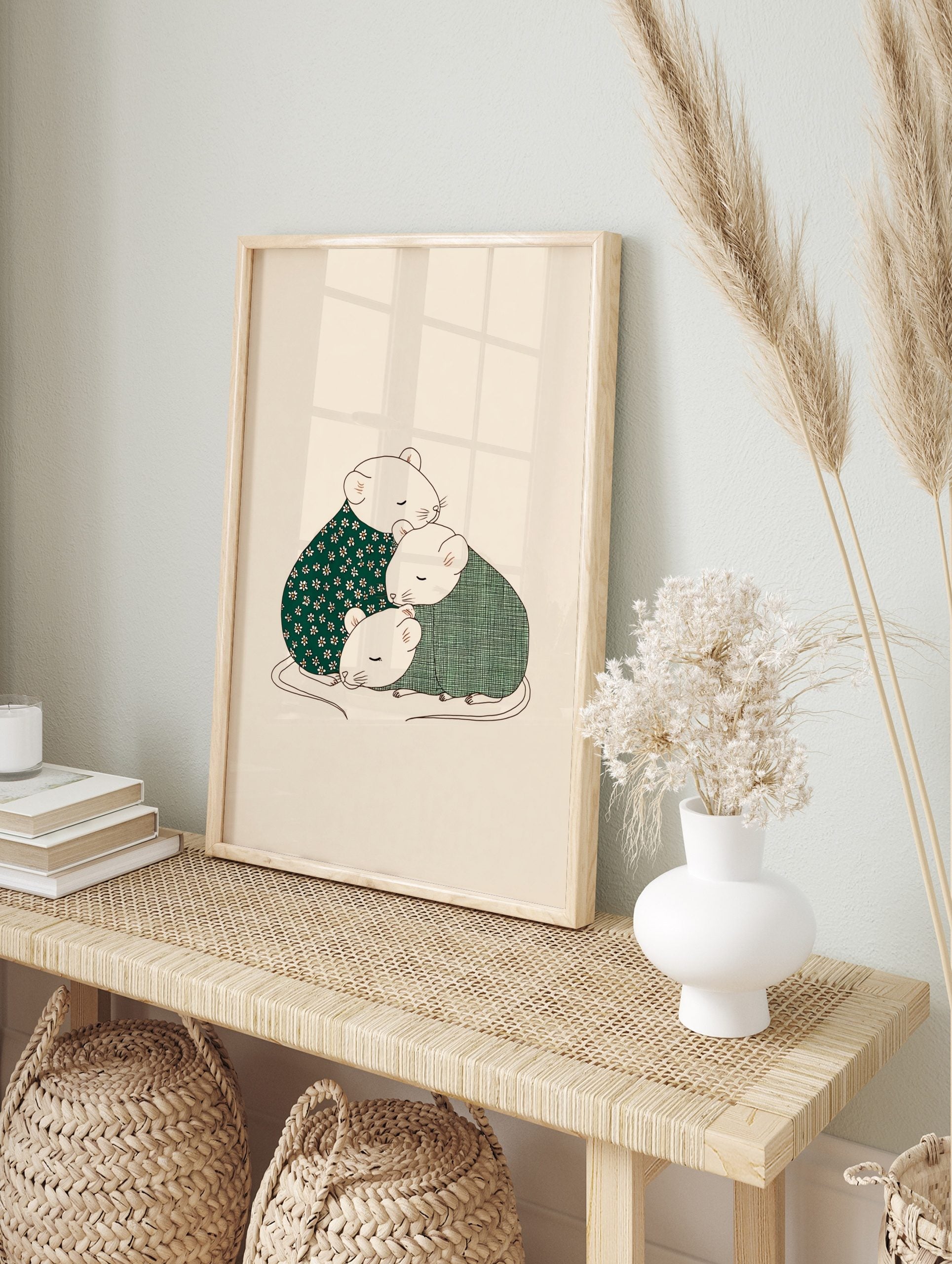 Illustration of three cosy mice huddled together, one in floral green, two in green plaid, on, in an alternate framed mockup