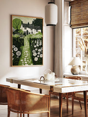 Cottage garden green linocut print with house, stone path, picket fence, foxgloves, and allium, in a styled room mockup