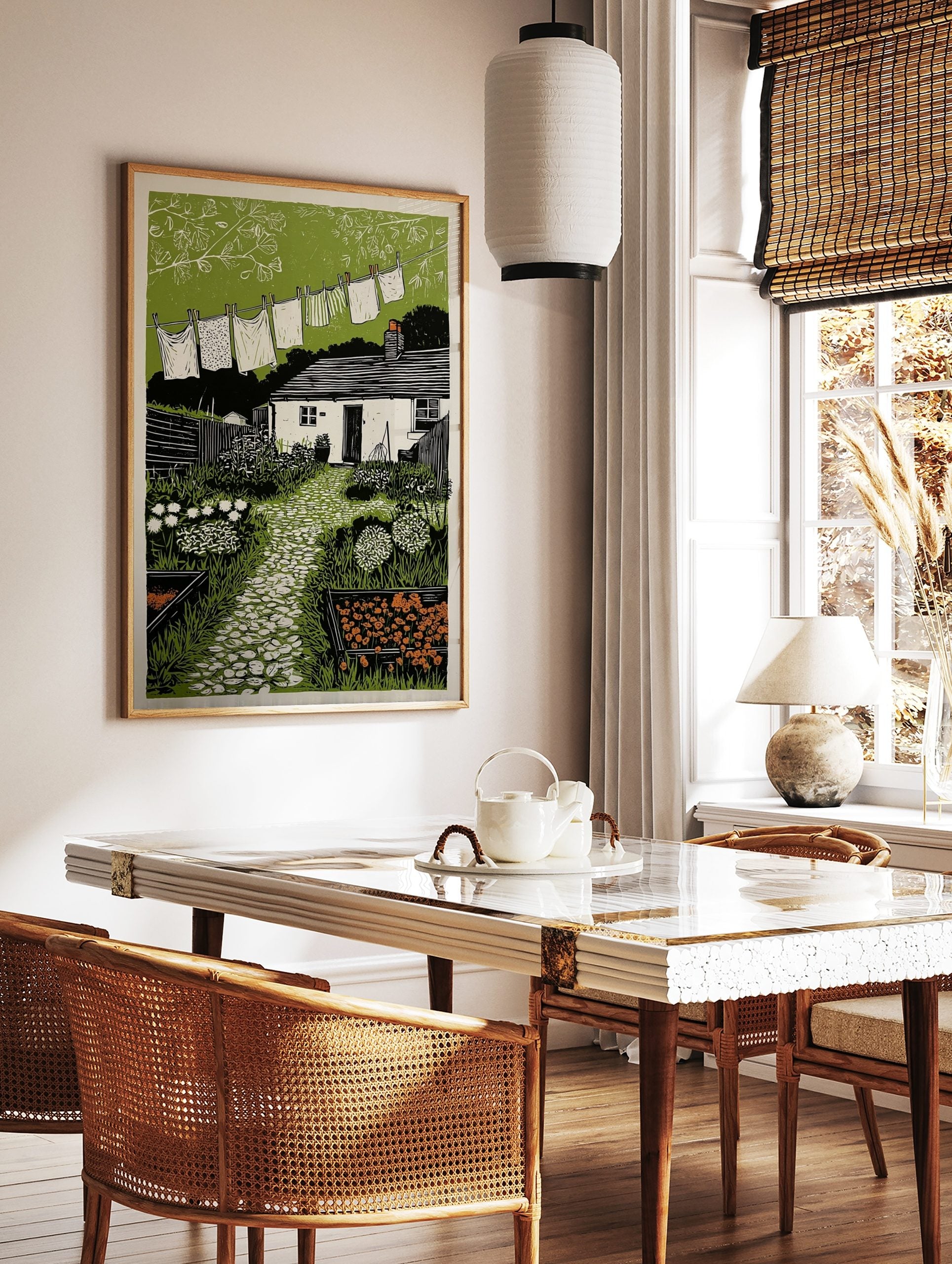 Linocut print of a cottage garden with washing line, white house, green plants, and stone path, in a styled room mockup