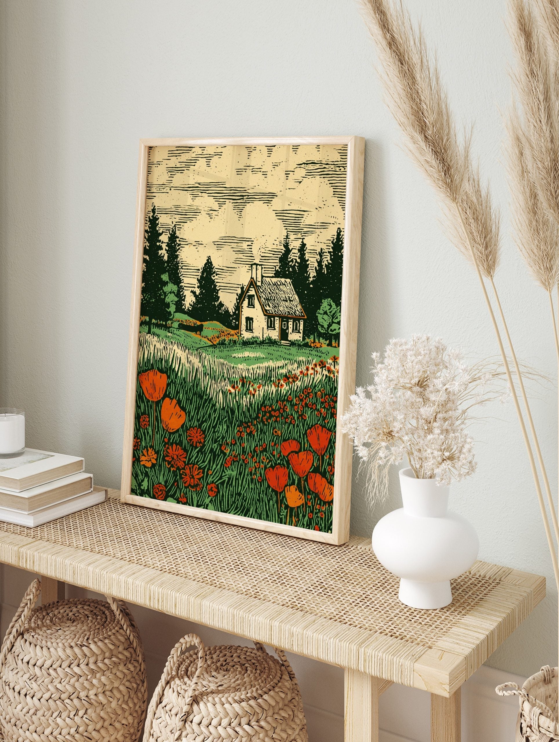 Woodcut print of a white cottage in a field of red poppies and tall green grass with pine, in an alternate framed mockup