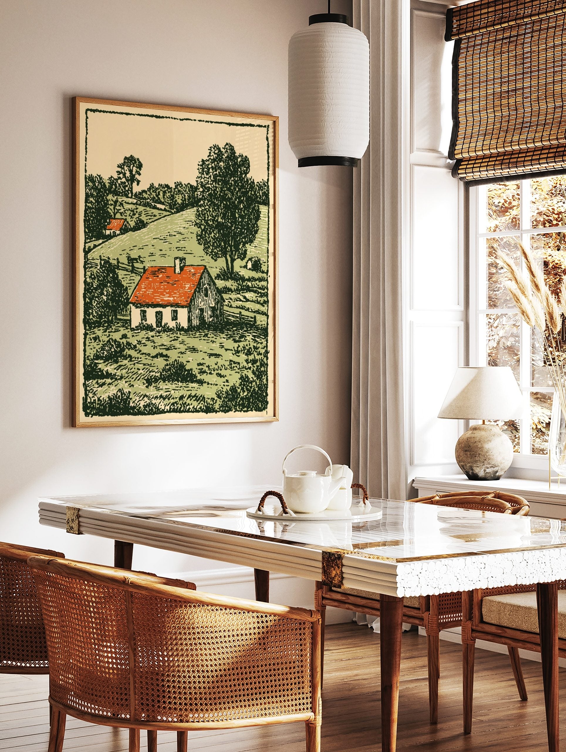 Woodcut style print of a white farmhouse with a red roof in a green, hilly countryside landscape, in a styled room mockup