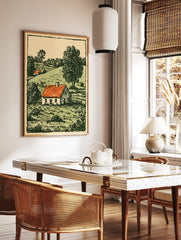 Woodcut style print of a white farmhouse with a red roof in a green, hilly countryside landscape, in a styled room mockup