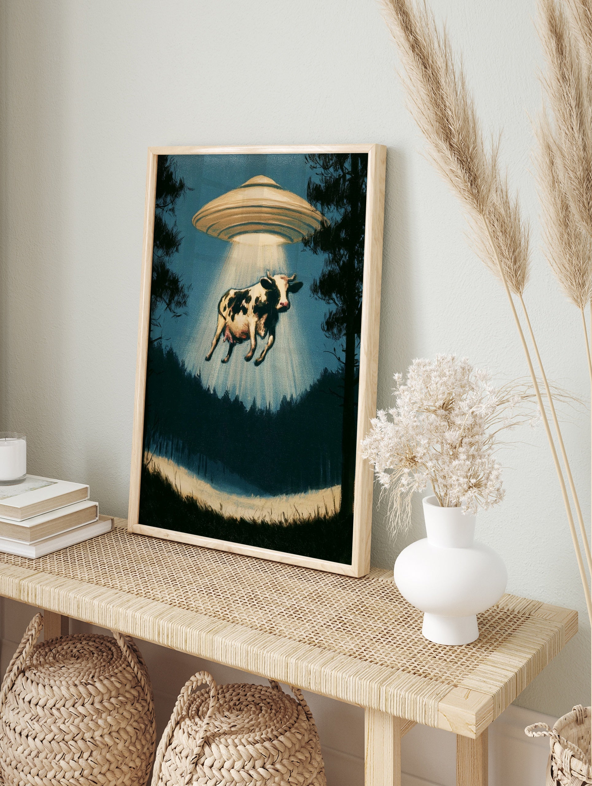 Surreal cow abduction wall art print featuring a UFO in a silhouetted forest with a glowing, in an alternate framed mockup