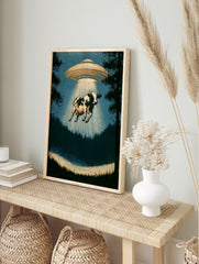 Surreal cow abduction wall art print featuring a UFO in a silhouetted forest with a glowing, in an alternate framed mockup
