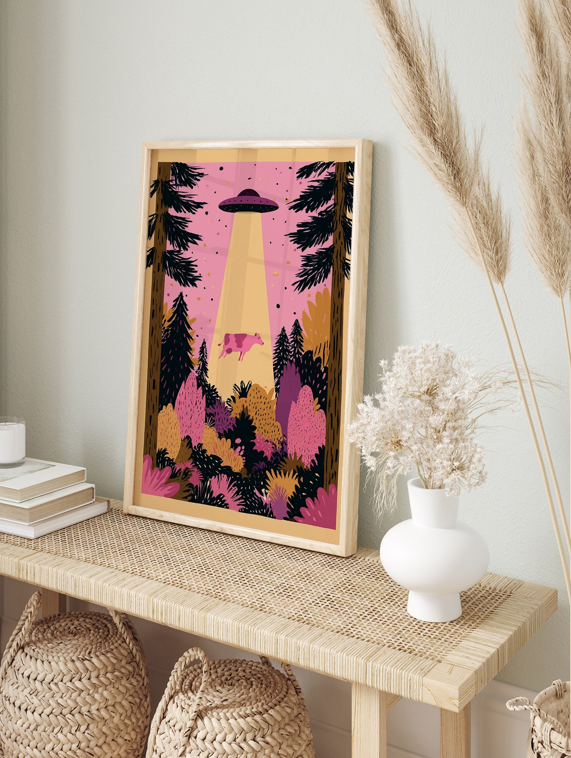 Illustrative pink cow being abducted by a UFO in a forest with pine trees and pink sky, in an alternate framed mockup