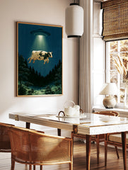 Surreal cow abduction wall art print featuring a UFO lifting a cow above a dark forest at night, in a styled room mockup