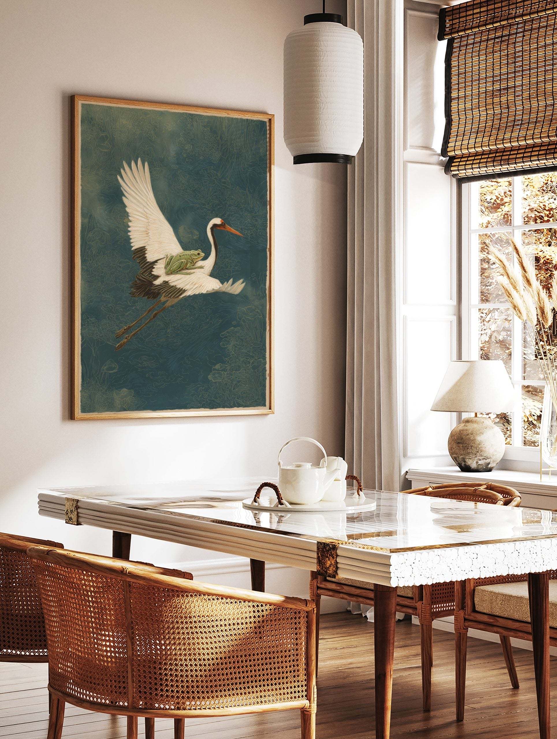 Illustrative art print of a white crane flying with a green frog on its back, over a deep blue, in a styled room mockup