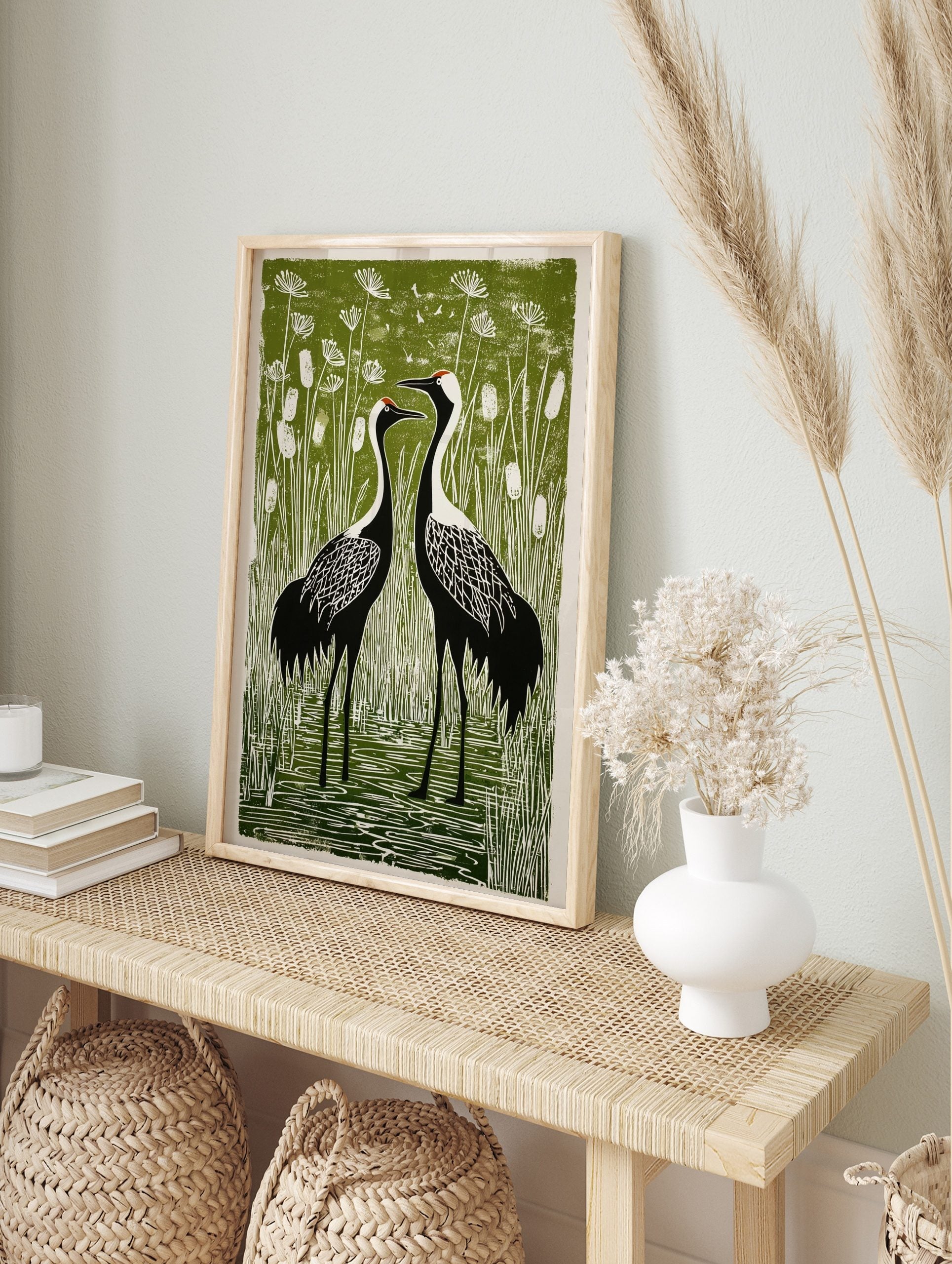 Linocut style print of two black and white crane birds with red crowns in a green marsh with, in an alternate framed mockup