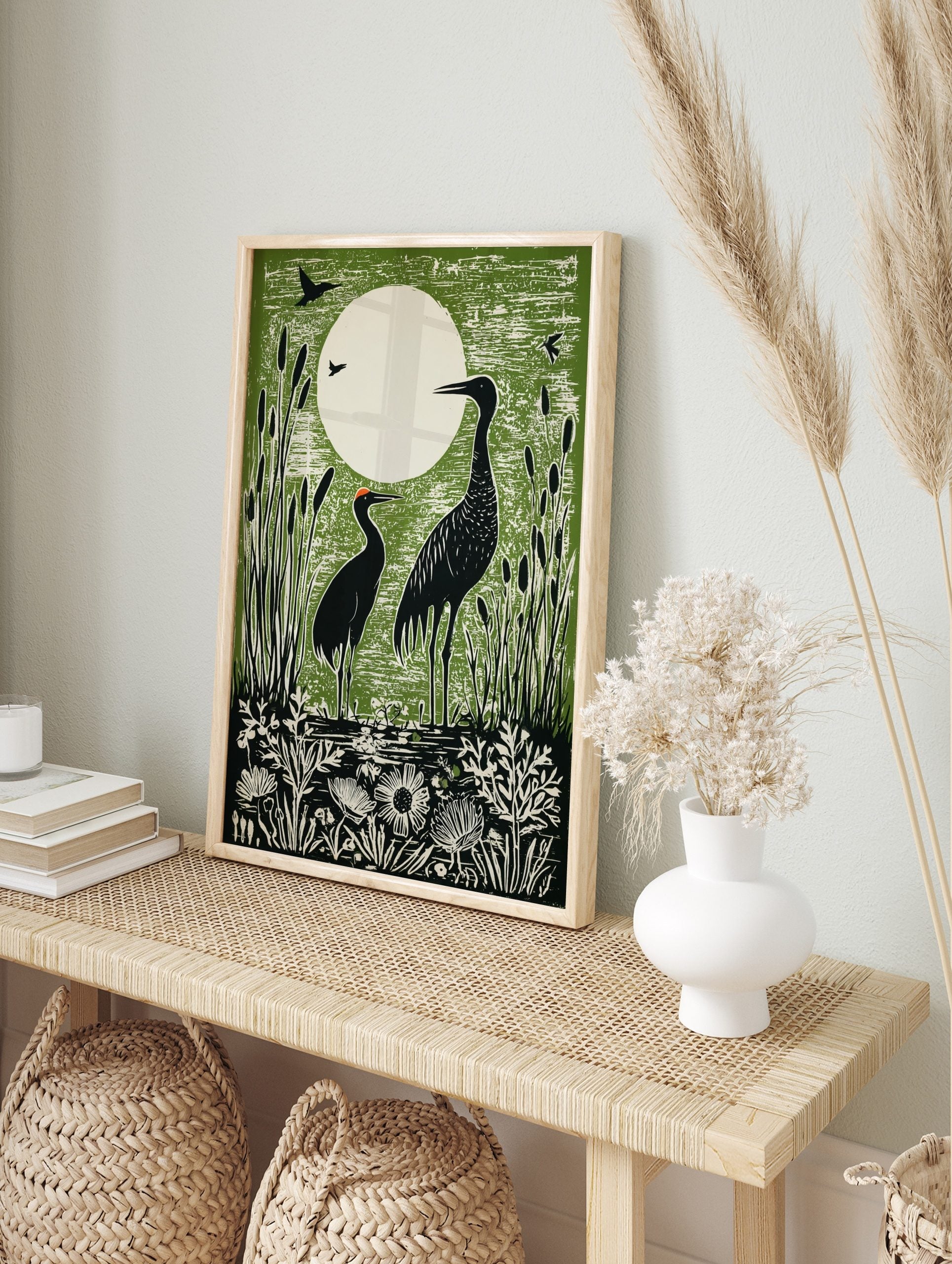 Green linocut print of two black cranes in a marsh with cattails and a large white moon in, in an alternate framed mockup