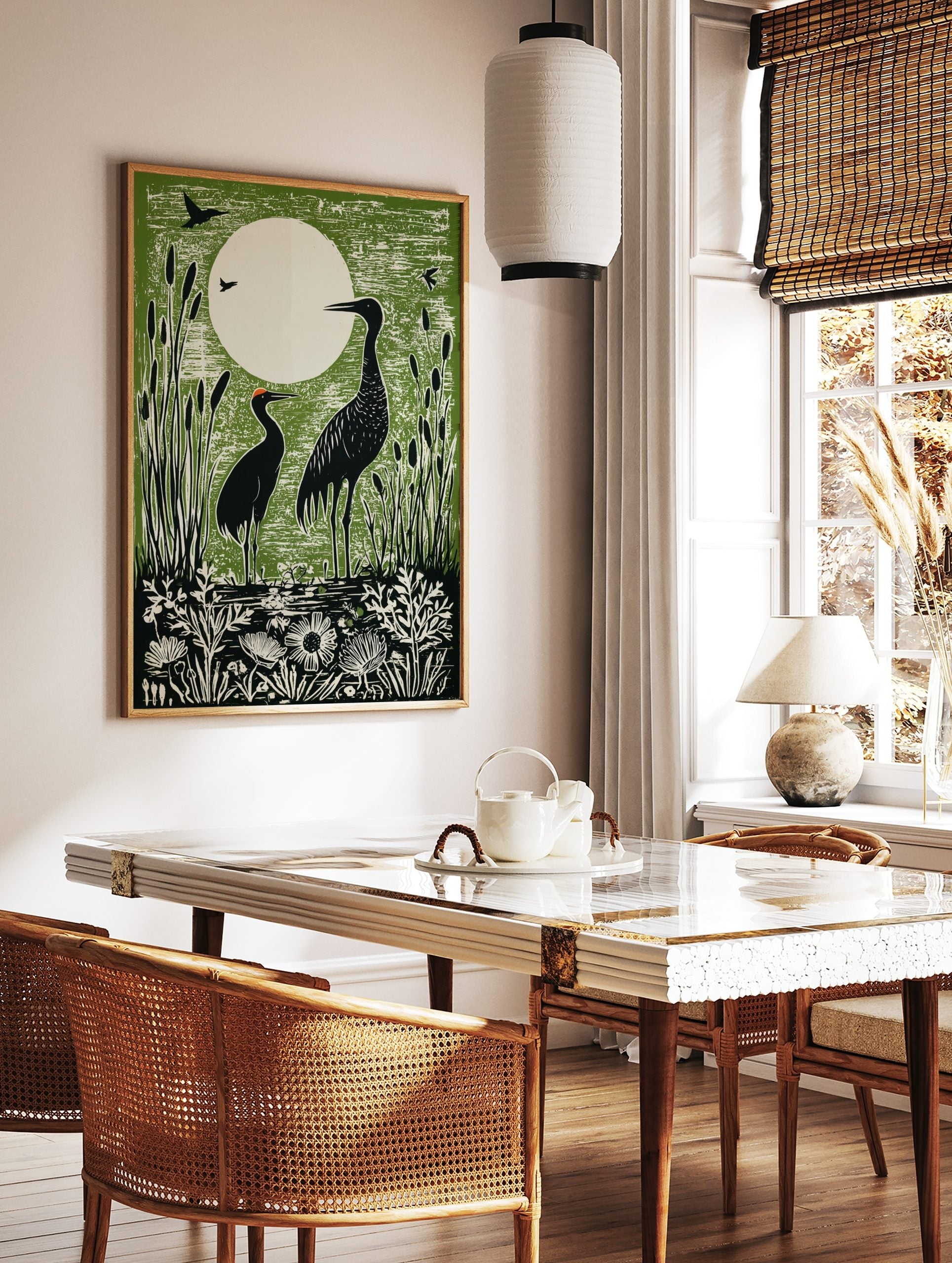 Green linocut print of two black cranes in a marsh with cattails and a large white moon in the, in a styled room mockup