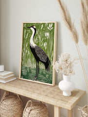 Linocut-style art print of a black and white crane with red head patch in green wetland with, in an alternate framed mockup