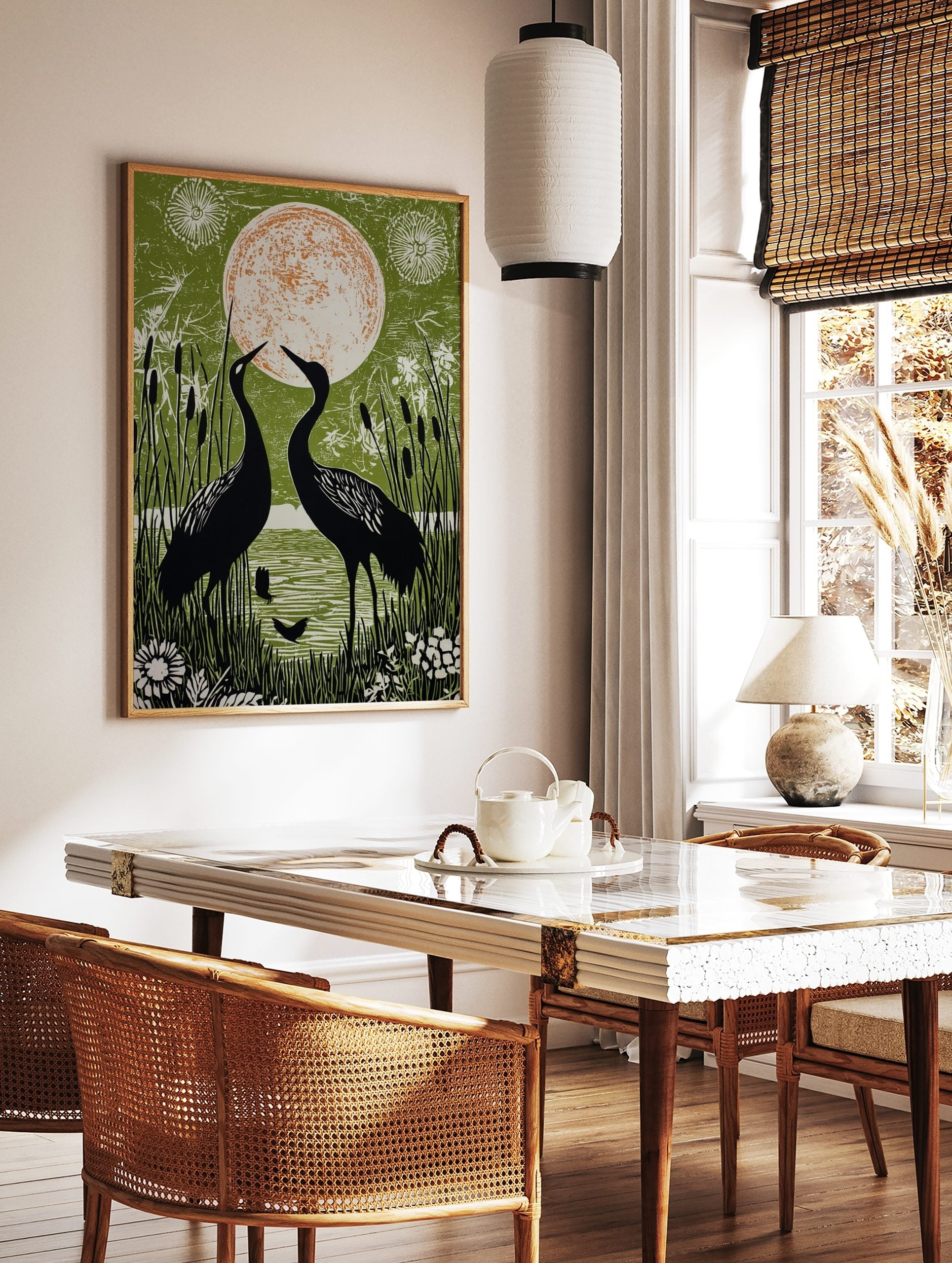 Two black cranes facing a large orange and white moon, surrounded by green reeds and water in an, in a styled room mockup