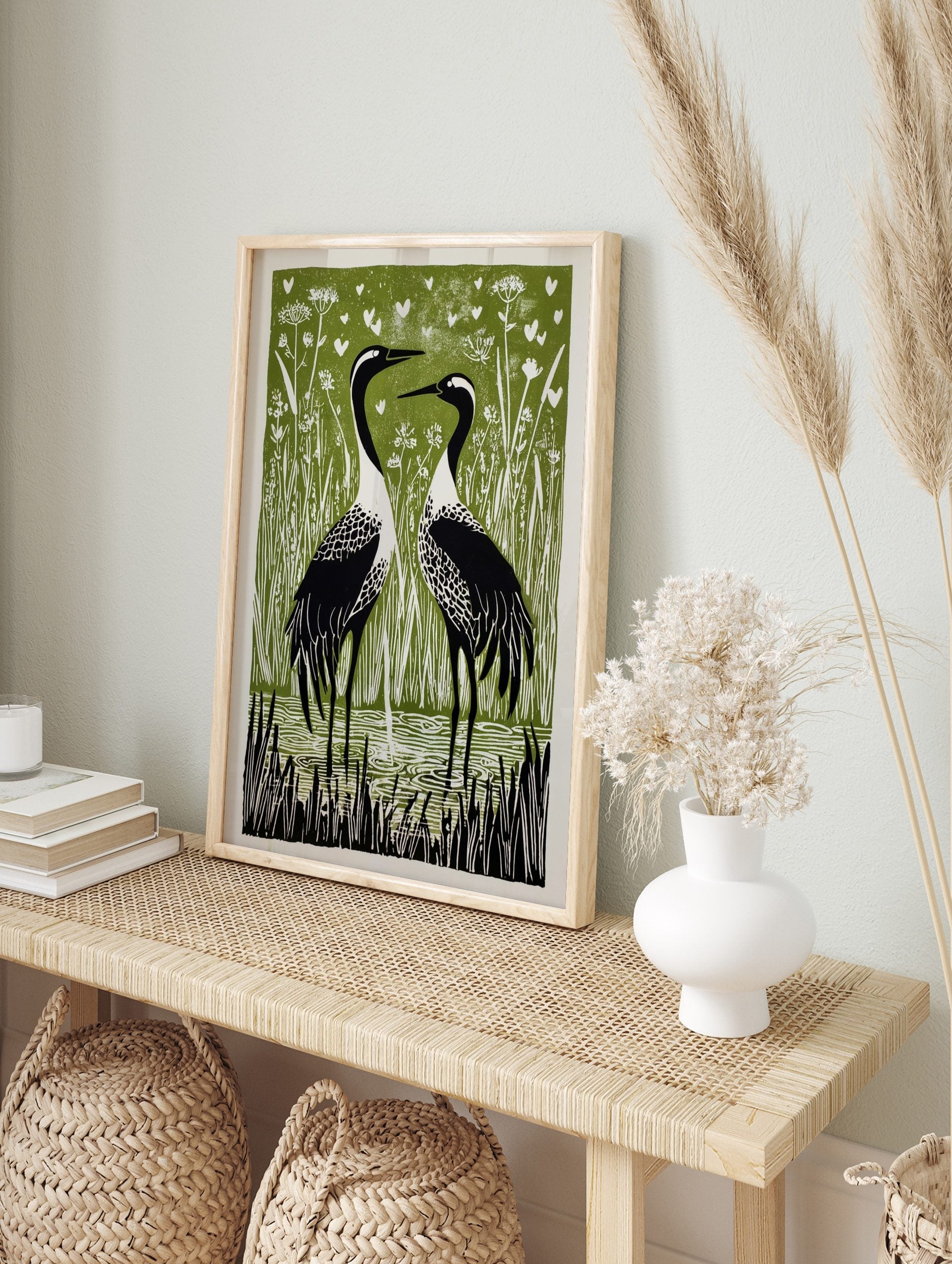 Two black and white cranes in reeds and water, with white hearts on a green background, in a, in an alternate framed mockup