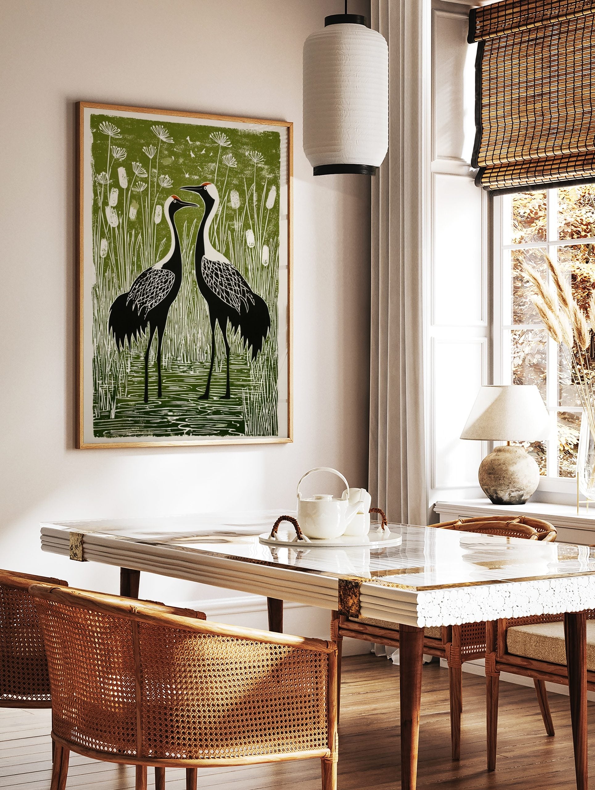Illustrative linocut-style print of two black and white cranes in a green wetland with cattails and, in a styled room mockup