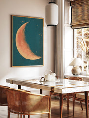 Crescent moon illustration with stippled orange-red surface and cream edge against a deep teal, in a styled room mockup