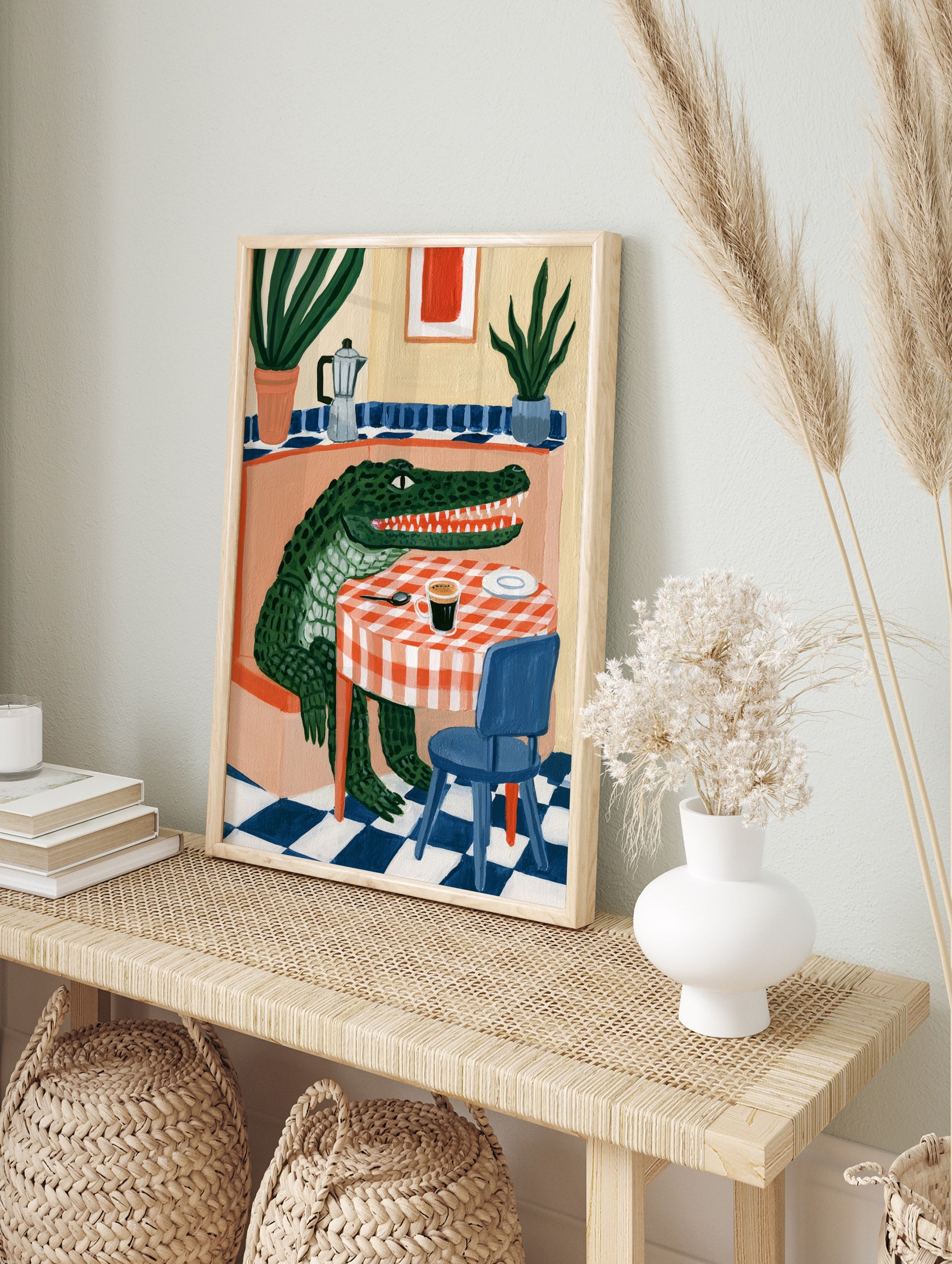 Green crocodile sitting at a table with coffee and a moka pot, illustrative style wall art, in an alternate framed mockup