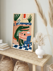 Green crocodile sitting at a table with coffee and a moka pot, illustrative style wall art, in an alternate framed mockup