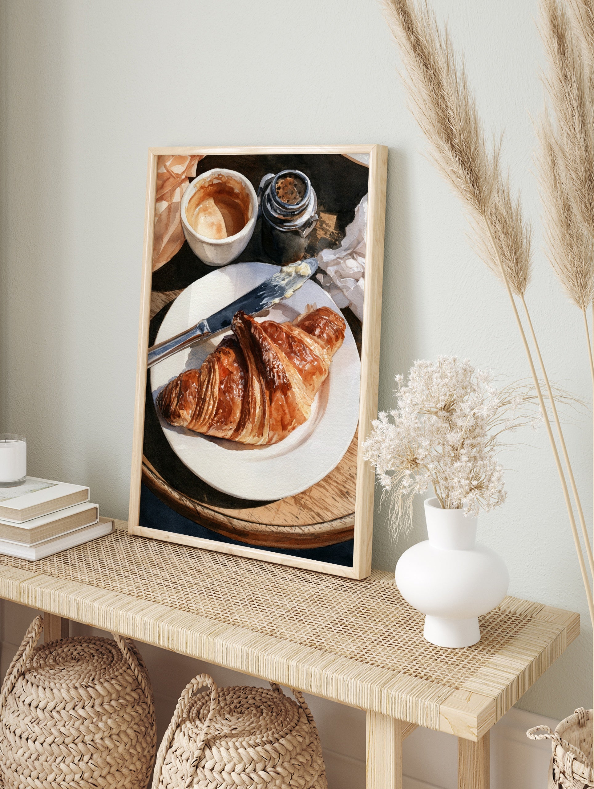 Watercolor painting of a croissant on a plate with coffee and a butter knife on a wooden, in an alternate framed mockup