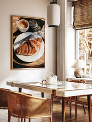 Watercolor painting of a croissant on a plate with coffee and a butter knife on a wooden table, in a styled room mockup