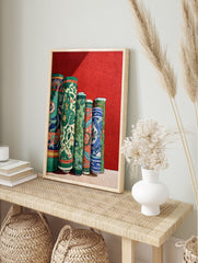 Cultural wall art print depicting several vibrantly patterned, rolled green, blue, and orange textiles against a red wall. - Image 3