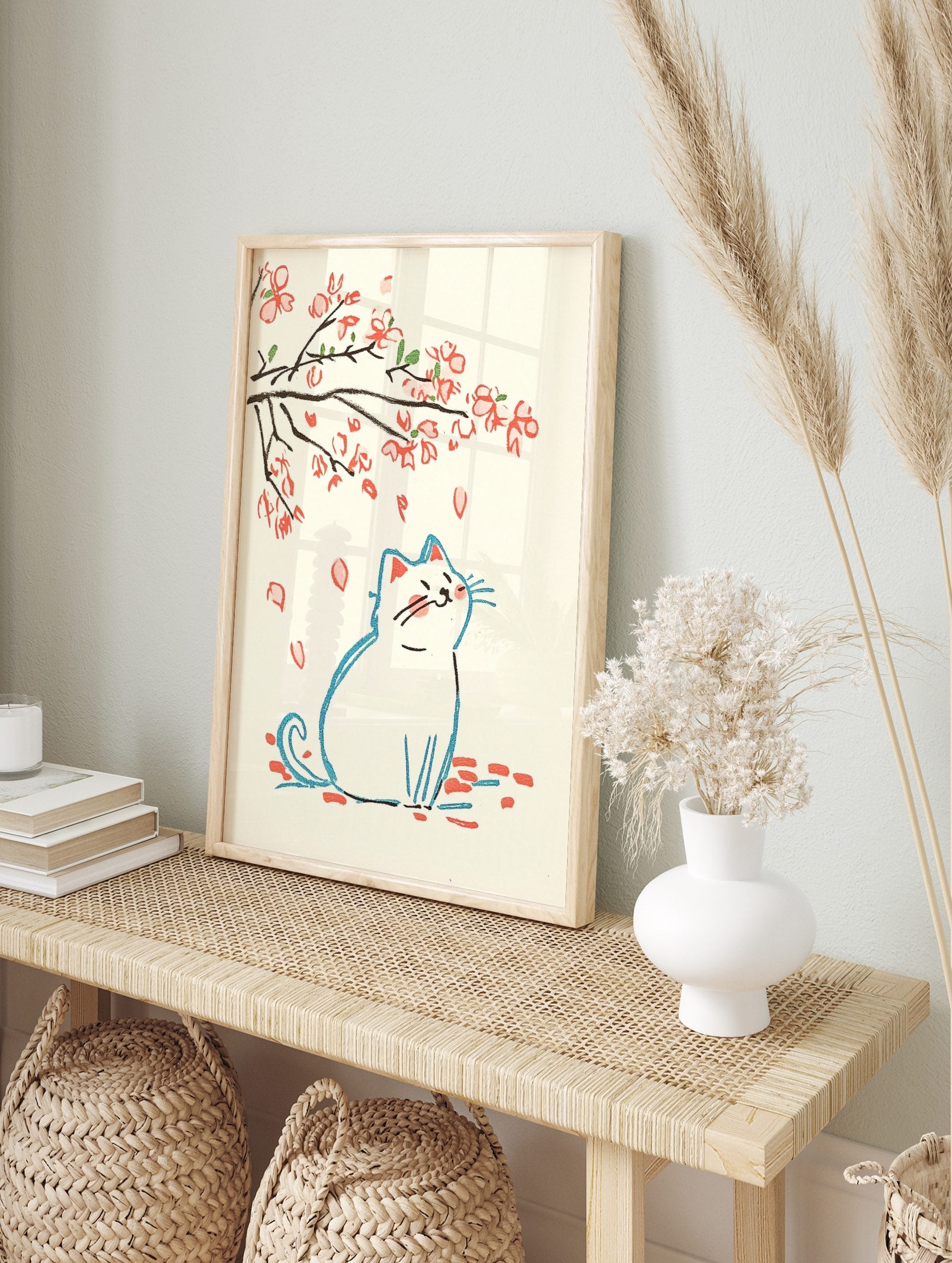 Illustrative print of a white cat looking up at falling pink cherry blossom petals and, in an alternate framed mockup