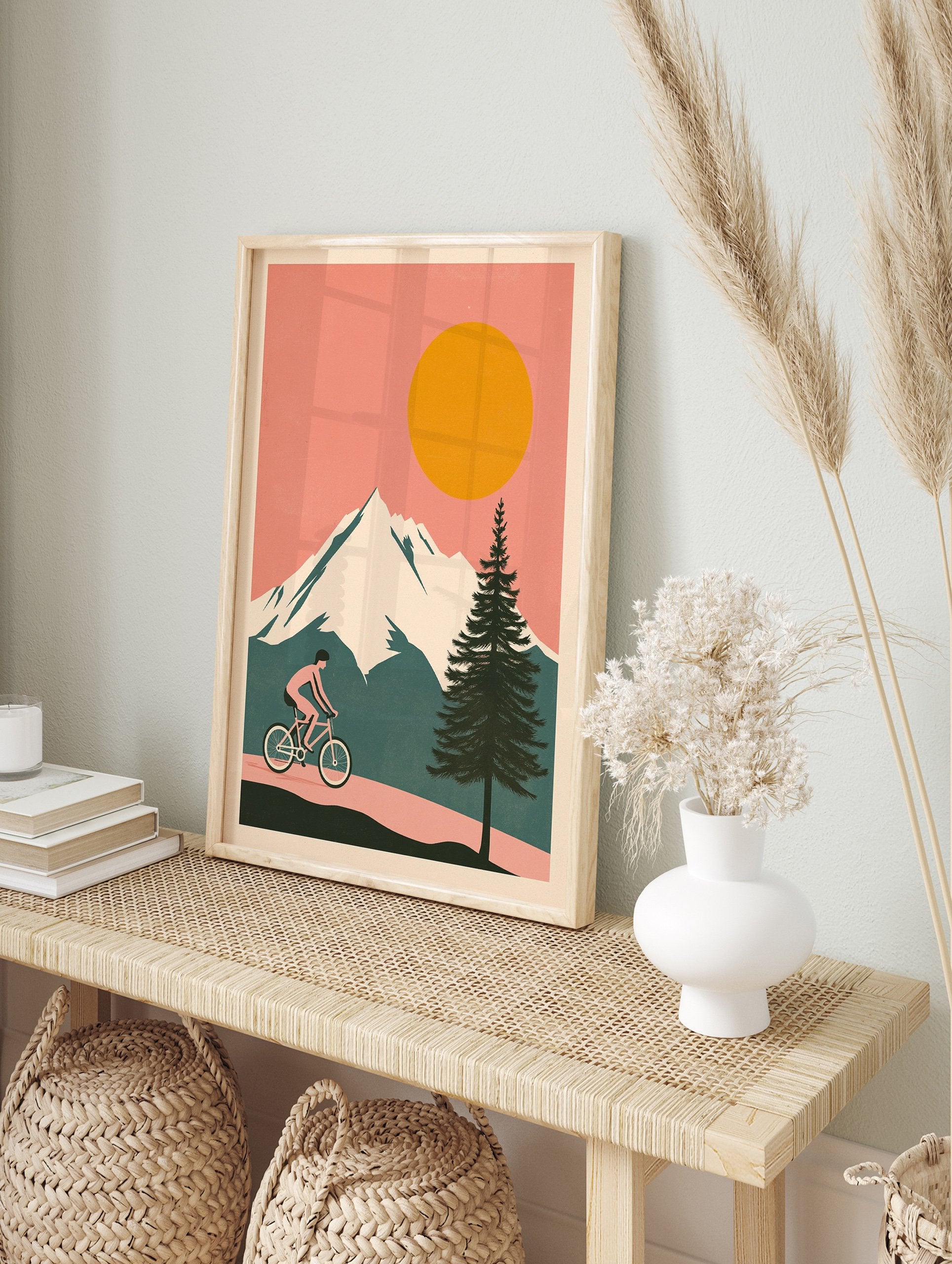 Cycling wall art illustration of a person riding a bicycle on a path with snowy mountains, a large orange sun, and a pine tree. - Image 3