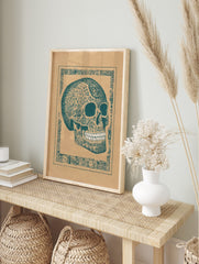 Decorated skull art print with intricate teal patterns on brown paper, framed by an ornate, in an alternate framed mockup