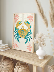 Decorative crab illustration wall art in golden yellow and teal blue with pink flowers on an, in an alternate framed mockup
