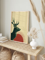 Illustrative green deer with antlers in profile against red sun on textured beige background, in an alternate framed mockup