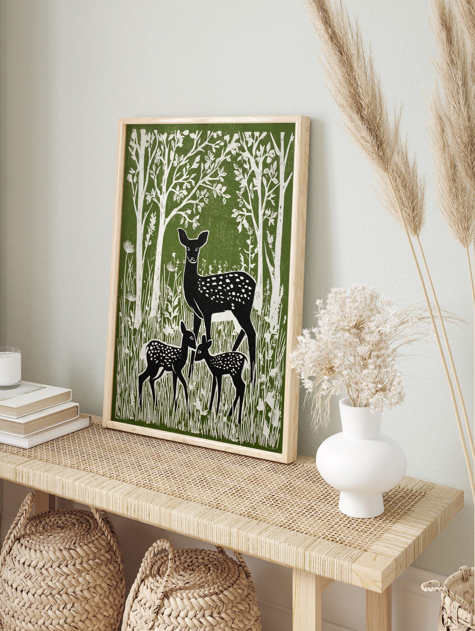 Green and white linocut style print of a mother deer and two fawns in a forest with tall trees, in an alternate framed mockup