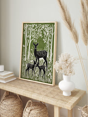 Green and white linocut style print of a mother deer and two fawns in a forest with tall trees, in an alternate framed mockup