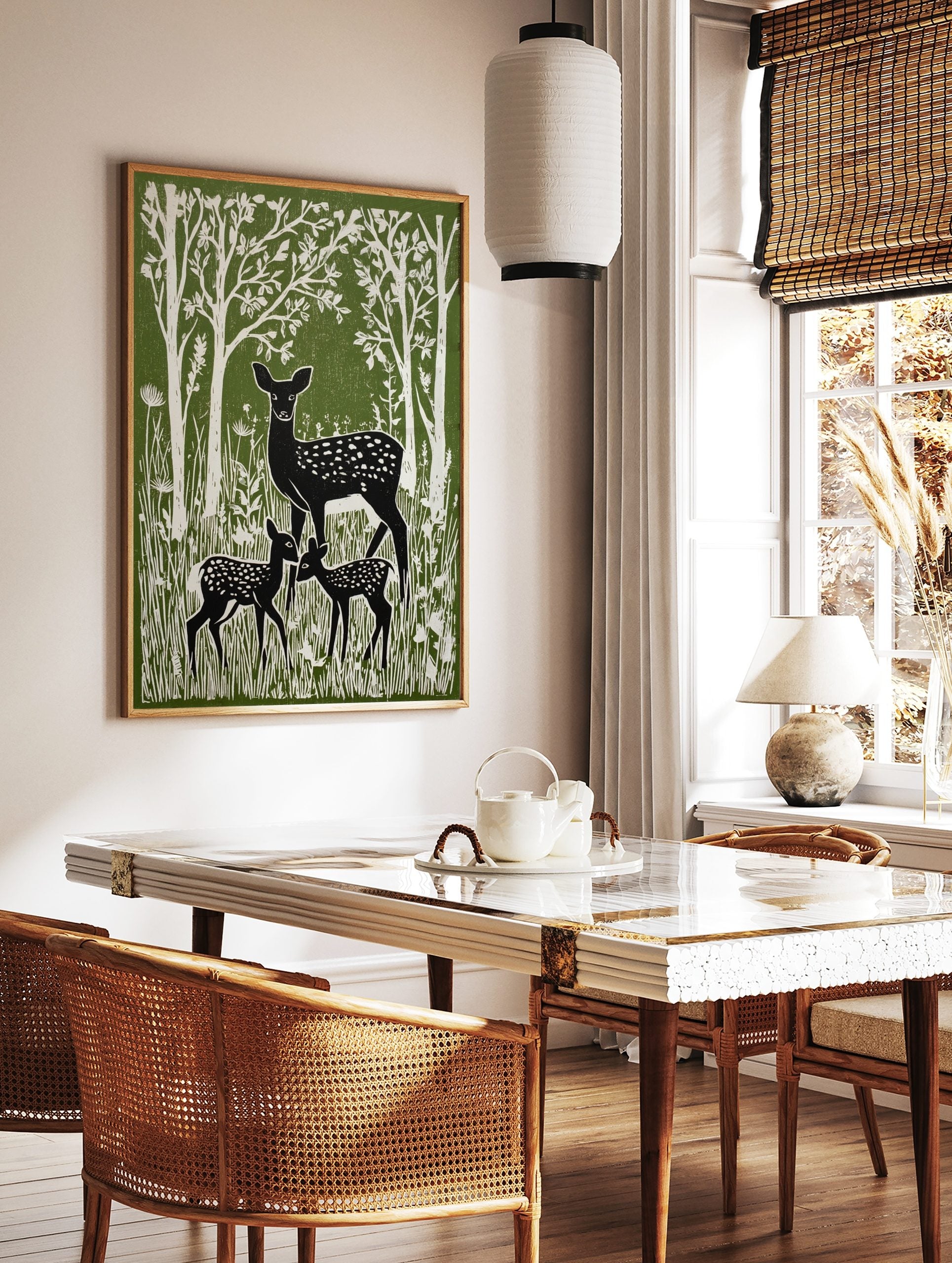 Green and white linocut style print of a mother deer and two fawns in a forest with tall trees, in a styled room mockup