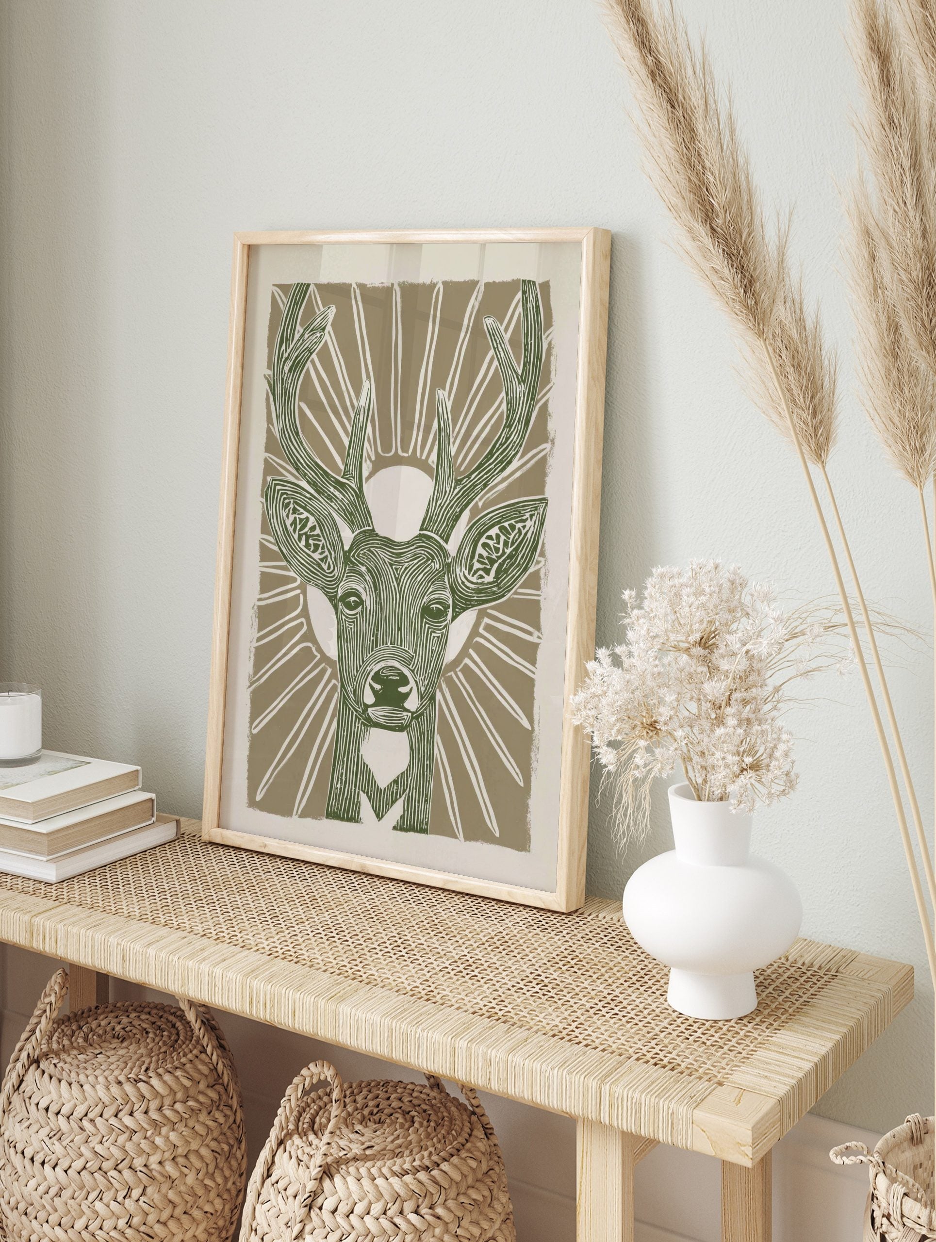 Stylised green deer head with antlers and sunburst on beige background, linocut style animal, in an alternate framed mockup