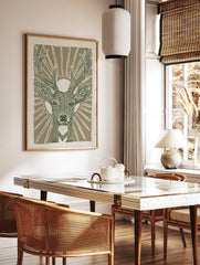 Stylised green deer head with antlers and sunburst on beige background, linocut style animal print, in a styled room mockup