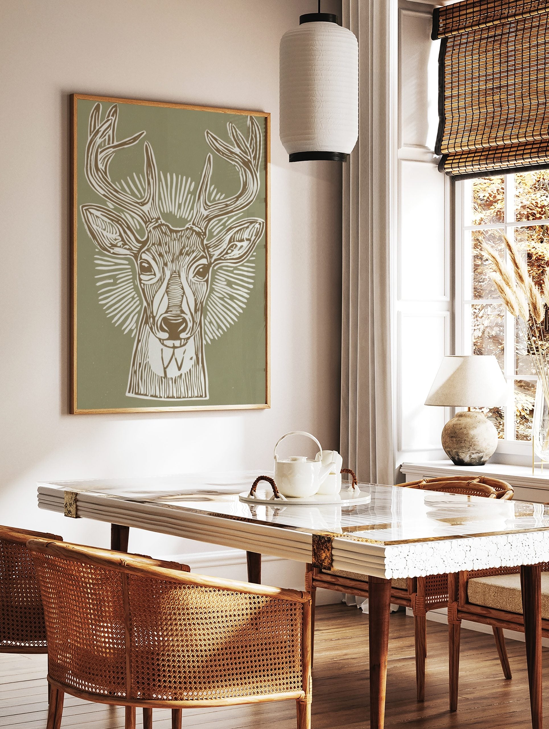 Illustrative deer head print with antlers and radial lines on a sage green background, in a linocut, in a styled room mockup