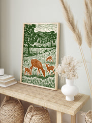 Woodcut style print of a spotted doe and three fawns grazing in a green meadow with trees and, in an alternate framed mockup