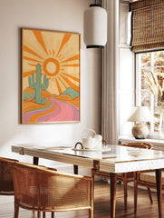 Retro desert landscape art print with a large teal cactus, orange sun, and a winding pink and, in a styled room mockup