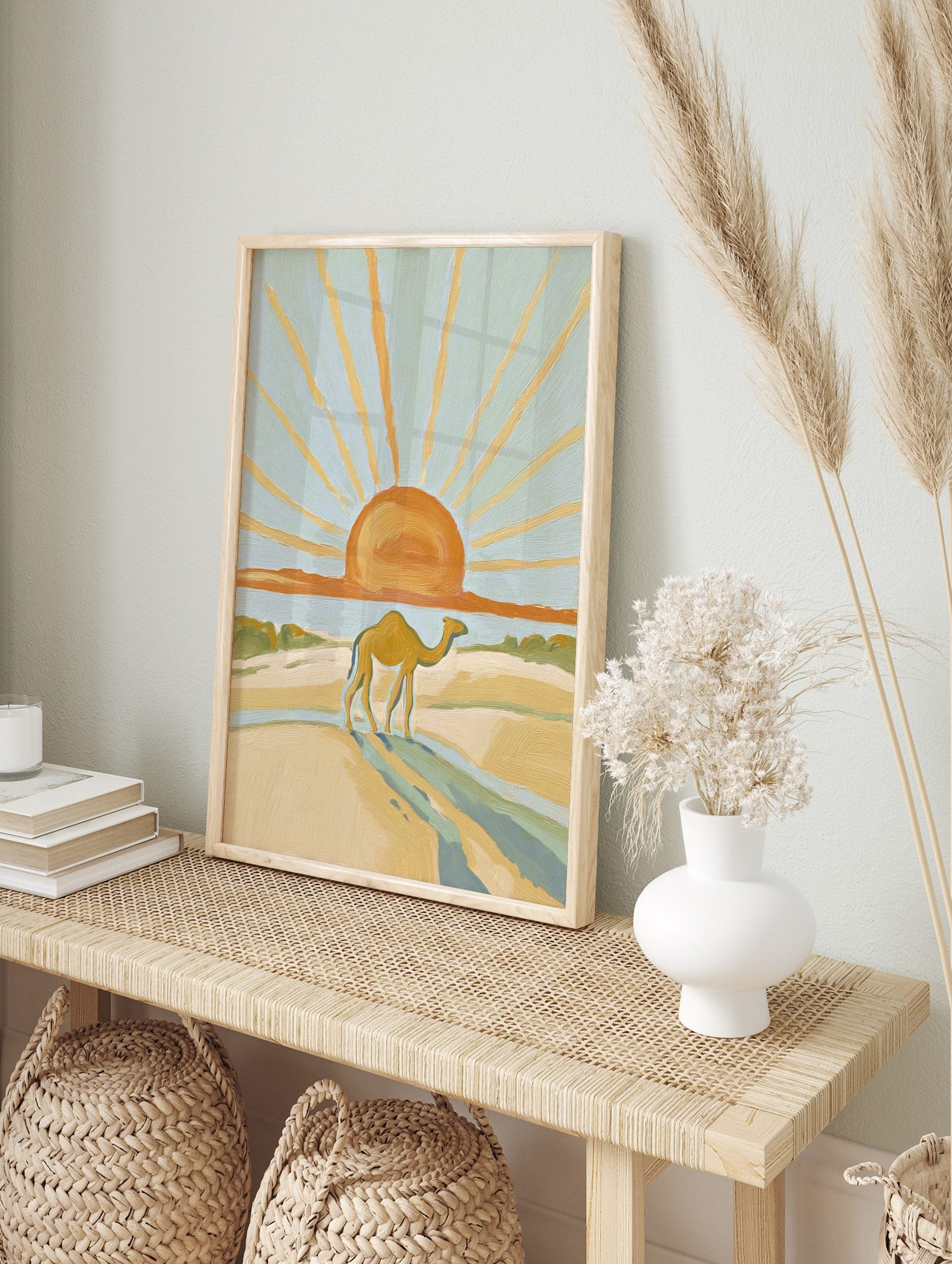 Illustrative desert scene with a camel walking on sand dunes under a large orange sun with, in an alternate framed mockup