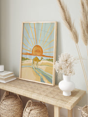 Illustrative desert scene with a camel walking on sand dunes under a large orange sun with, in an alternate framed mockup