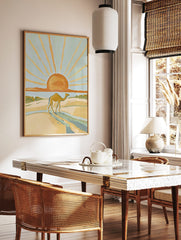 Illustrative desert scene with a camel walking on sand dunes under a large orange sun with golden, in a styled room mockup